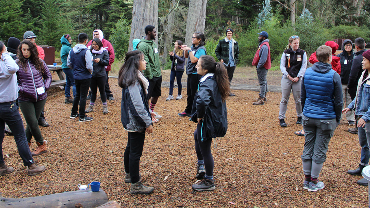 Learning to lead overnight activities at a leadership training at Rob Hill Campground A large group of people stand outside in pairs and speak to their partners during a leadership training
