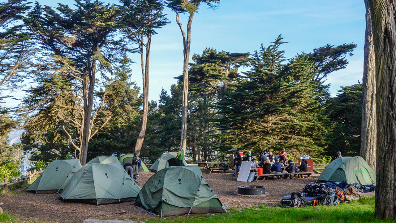 Having lunch at Rob Hill Campground A group of adults sit outside on a sunny day eating lunch at a picnic bench under eucalyptus trees while surrounded by camping tents
