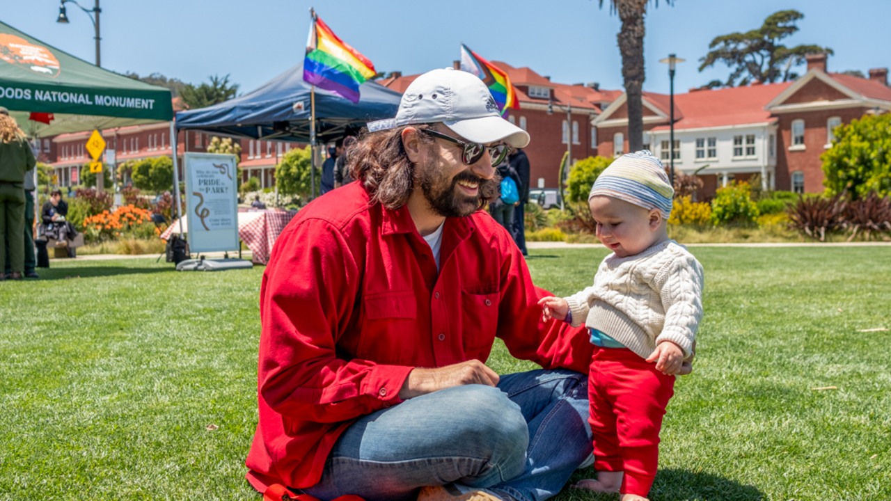 PRSF_20240601_DAH_050_2x1.jpg A father and child sit on the Presidio lawn during Pride at the Presidio event.
