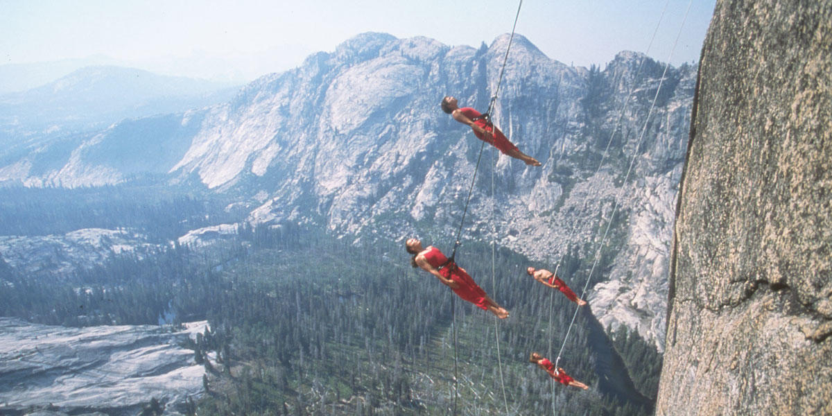four people suspended from safety harnesses propel themselves away from the granite face of rock wall