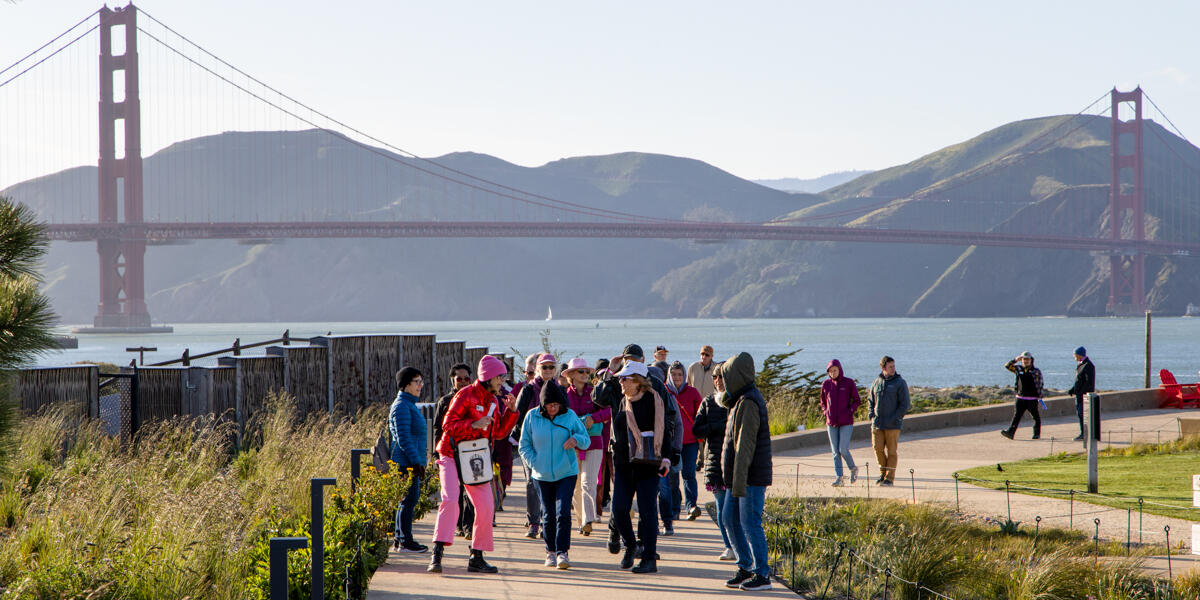 A group of event participants on a walking tour of the Presidio Tunnel Tops. Golden Gate Bridge and Marin Headlands are seen in the background.