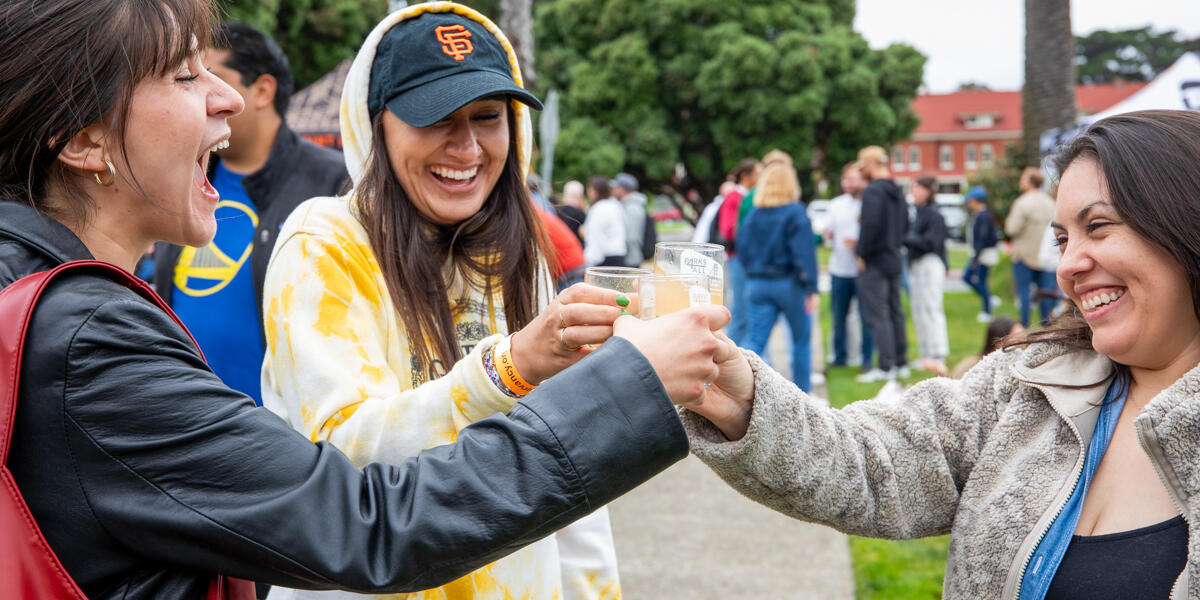 Three smiling and laughing women raise their glasses at the Parks4All: Brewfest in the Presidio