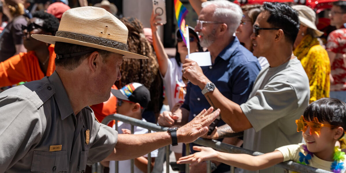 A ranger high fives a child wearing orange star sunglasses at the 2024 SF Pride Parade.