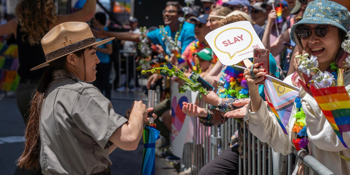 A ranger interacts with an excited crowd that's holding rainbow flags, cellphones, and a sign that says "SLAY".