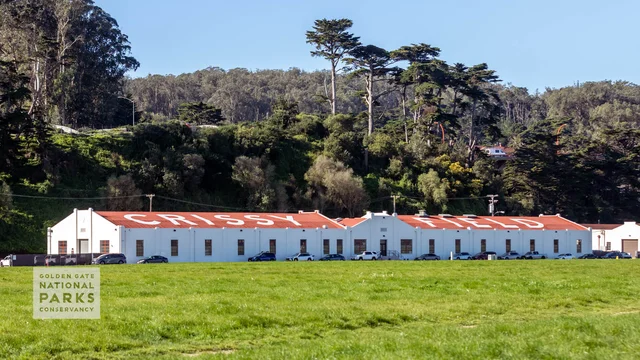A scenic photo from the lawn of Crissy Field of the hangar building with bold le