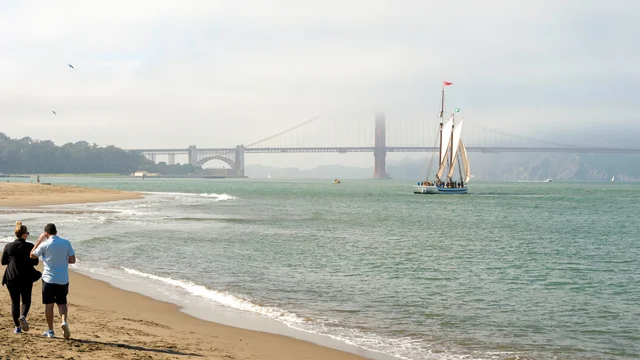 The sun breaks through a hazy day at Crissy Field East Beach, two park goers wal