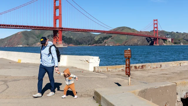 A parent and toddler walking hand in hand by the waterfront near the Warming Hut
