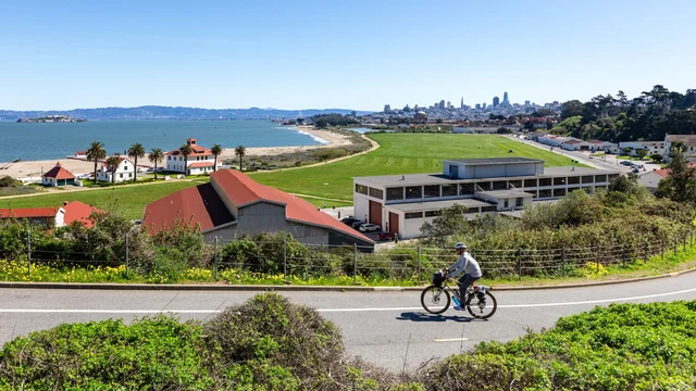 A cyclist is seen biking up a road with a vast backdrop of Crissy Field and the 