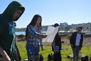A group of four high school students stand in a line outdoors while leading a presentation about the natural environment 