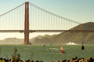Windsurfers cruise across bay waters with the Golden Gate Bridge spanned across the background.