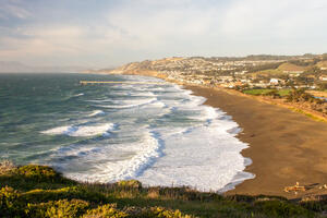 An expansive view of the coastline in Pacifica, CA from Mori Point. A long fishing pier stands out over the beach.