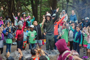 A National Park Service Ranger leads a large group of smiling children in an interactive story