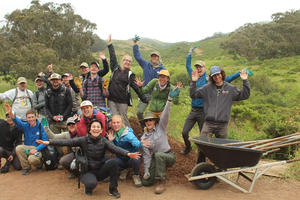 A group of volunteers joyfully pose after working outside on a trail