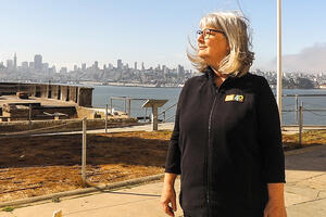 Nicki Phelps stands on Alcatraz Island with a view of San Francisco behind her.