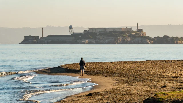 A park visitor walks along Crissy Field East Beach with a view of Alcatraz in th