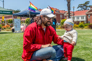 A father and child sit on the Presidio lawn during Pride at the Presidio event.