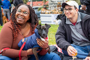 A smiling couple sits with their dog at the Parks4All: Brewfest in the Presidio