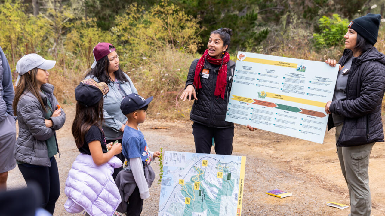 Community Engagement in Rancho Corral de Tierra Two Golden Gate National Parks Conservancy community engagement staff members presenting an infographic sign to local community group visitors of Rancho Corral de Tierra.