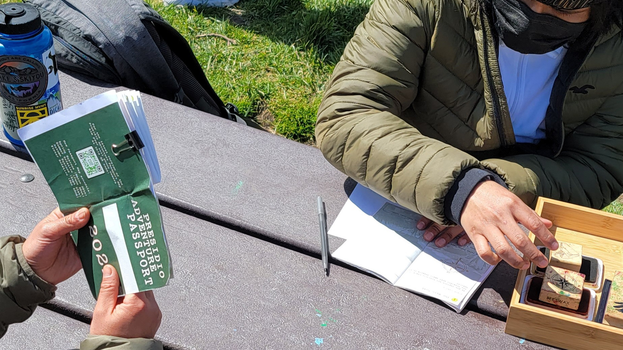 adventure_guides_2021.jpg Adventure Guides sit at a park bench, stamping Presidio Adventure Passports.