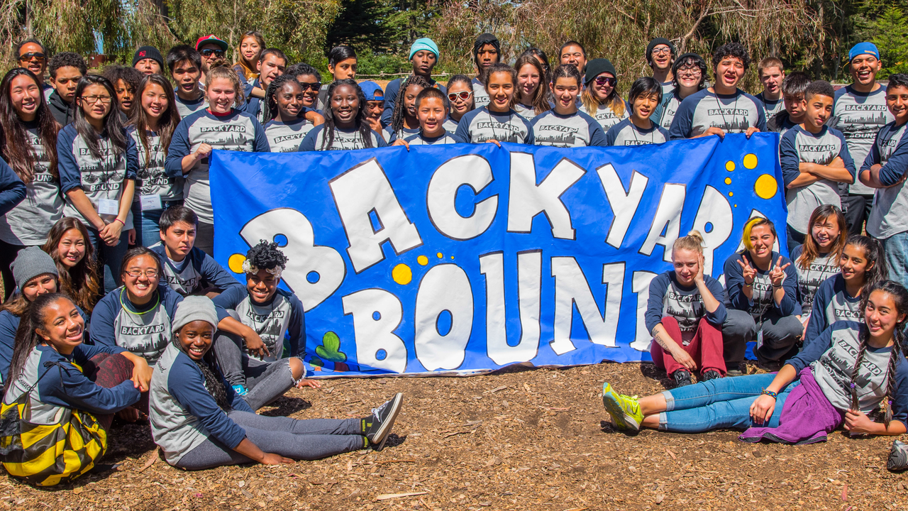 Backyard Bound Youth Summit Group Photo A large group of youth and youth workers gather around a banner reading Backyard Bound
