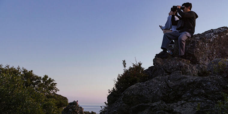 A person looks through binoculars while sitting on a rock on Mt. Tamalpais.