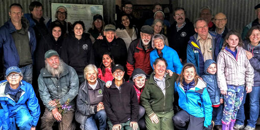 A large group smiles while posing for a photo in front of a metal barn.