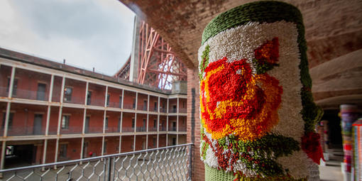 Pole covered in yarn with Fort Point and Golden Gate Bridge in background.